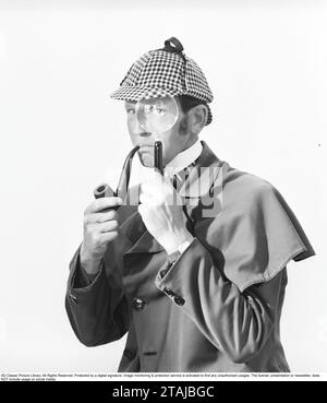 Jouer détective. Un homme vêtu de vêtements typiques comme le célèbre détective fictif Sherlock Holmes regarde la caméra à travers une loupe. Banque D'Images