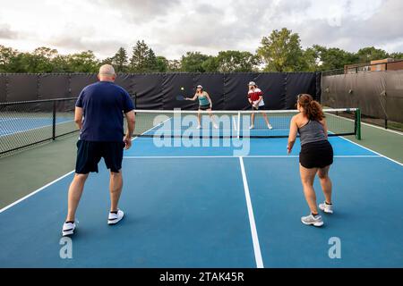 Une joueuse de pickleball renvoie une balle au filet tandis que son partenaire regarde dans un match de double mélange. Banque D'Images