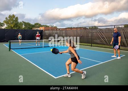 Une joueuse de pickleball retourne une balle tandis que son partenaire regarde dans un match de double mélange. Banque D'Images