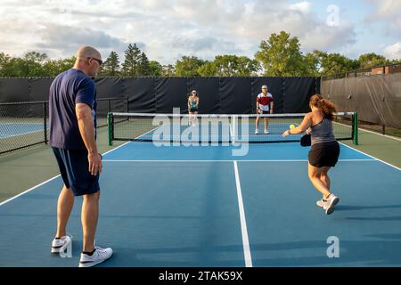 Une joueuse de pickleball renvoie une balle au filet alors que ses adversaires se préparent à retourner le coup. Banque D'Images