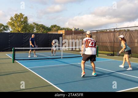 Une joueuse de pickleball renvoie une balle au filet alors que ses adversaires se préparent à retourner le coup. Banque D'Images