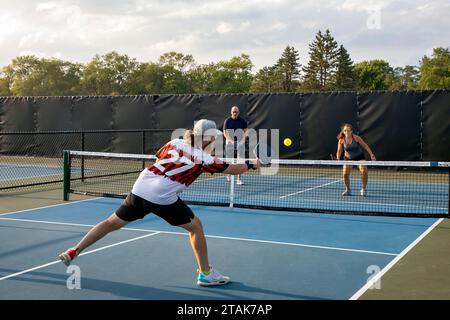 Un joueur de pickleball masculin renvoie un coup à ses adversaires qui approchent du filet. Banque D'Images