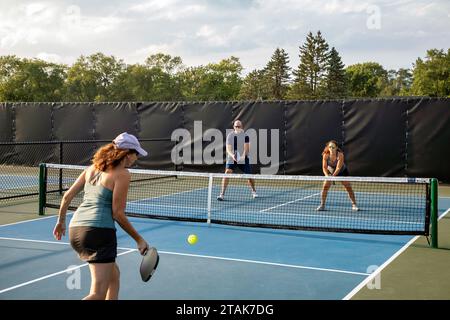 Une joueuse de pickleball renvoie une balle alors que ses adversaires se tiennent au filet pour une volée. Banque D'Images