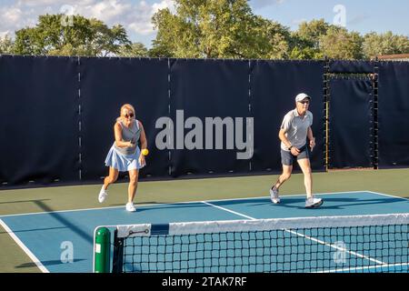 Une joueuse de pickleball de sexe féminin retourne un tir à la ligne de base alors que son partenaire masculin se déplace vers le filet. Banque D'Images