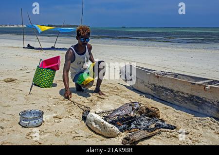 Homme malgache cuisinant du poisson fraîchement pêché sur grill sur feu de charbon de bois sur la plage de sable à Andavadoaka près de Morombe, région Atsimo-Andrefana, Madagascar Banque D'Images
