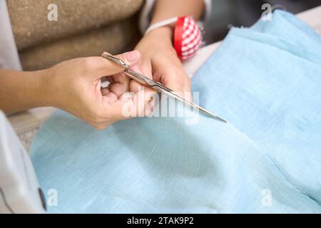 Gros plan de l'artisan coupe le tissu bleu avec des ciseaux Banque D'Images