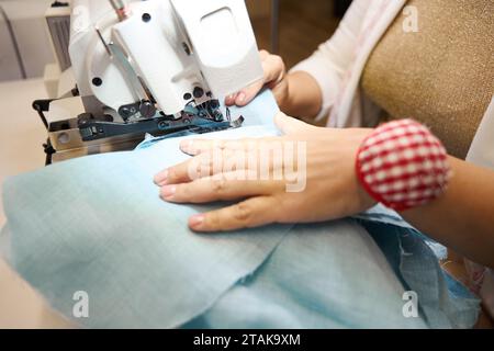 Lady travaille sur une machine à coudre avec un tissu bleu Banque D'Images