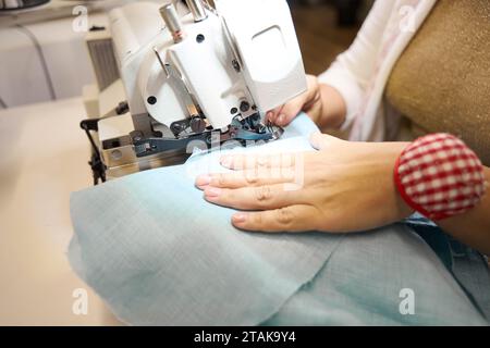 Couturière travaille sur une machine à coudre avec un tissu bleu Banque D'Images