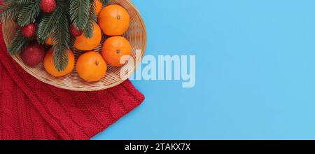 Mandarines dans un panier, une écharpe tricotée rouge et des branches de sapin sur fond bleu. Composition de Noël, nouvel an, bannière. Décor du nouvel an. Copier spa Banque D'Images