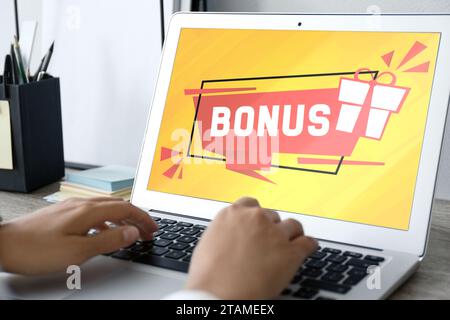 Gain de bonus. Femme utilisant un ordinateur portable à table, gros plan. Illustration de la boîte cadeau et mot sur l'écran de l'appareil Banque D'Images