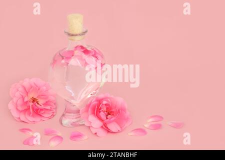 Parfum de fleur de rose avec des fleurs dans une bouteille en forme de coeur avec des pétales lâches sur rose. Produit de beauté floral naturel, cadeau pour la Saint Valentin, anniversaire, A. Banque D'Images