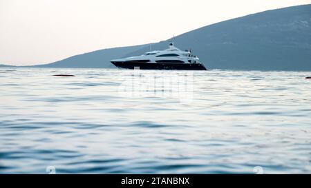 Luxueux yacht à moteur nageant à travers les vagues calmes de la mer au coucher du soleil. Vacances, vacances d'été et tourisme. Banque D'Images
