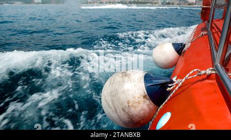 Gros plan des ailes, cordes et bouées accrochées sur le côté du bateau rouge naviguant dans la baie de mer. Banque D'Images