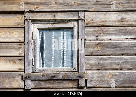 une vieille maison en bois avec une vitre en bois dans le mur et des rideaux derrière elle Banque D'Images