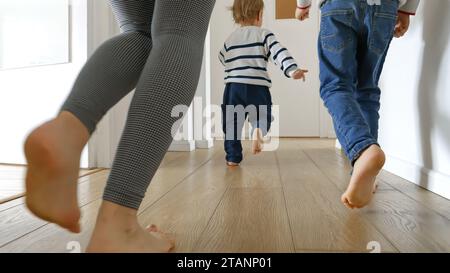 Gros plan de la mère et deux garçons courant sur le plancher de bois à la maison. Concept d'amour familial, de joie et de plaisir dans un ménage. Banque D'Images