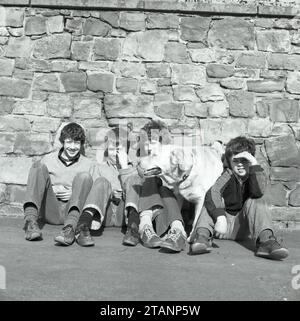 Un groupe de quatre garçons des années 1970 traînant seuls avec leur chien. Banque D'Images