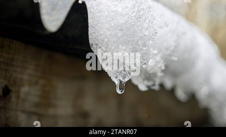 Gros plan de gouttelettes d'eau tombant de glaçons sur un toit. Essence du printemps et la transition de l'hiver, mettant en valeur la fonte de la neige Banque D'Images