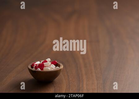 Bol en bois d'olive plein de pilules ou de capsules blanches rouges sur une table en bois avec espace de copie, mise au point peu profonde Banque D'Images
