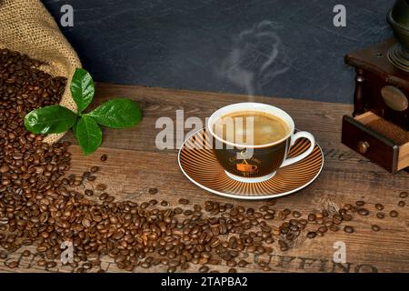 Kaffee Komposition mit Kaffeetasse, Kaffeebohnen in Kaffeesack, historischer Kaffeemühle und Kaffeeblätter auf einem Holztisch Banque D'Images