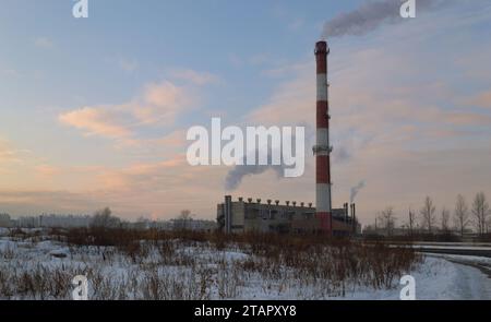 Chaufferie avec une grande cheminée à fumer rayée au milieu d'un paysage de soirée d'hiver Banque D'Images