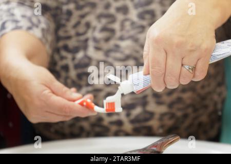 Gros plan des mains d'une femme mettant du dentifrice sur la brosse reflétée dans un miroir Banque D'Images