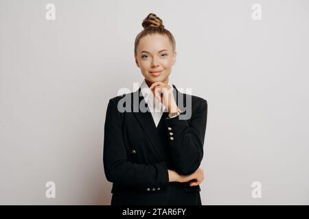 Femme professionnelle en blazer noir, pose de pensée, fond blanc Banque D'Images