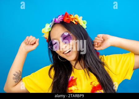 Photo de studio avec fond bleu d'une femme chinoise avec des lunettes de soleil et danse florale hawaïenne de couronne Banque D'Images