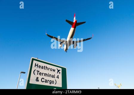 Avion à réaction de ligne en finale pour atterrir à l'aéroport de Londres Heathrow, Royaume-Uni, survolant le panneau de signalisation routière avec les indications pour Heathrow terminal 4 & Cargo Banque D'Images