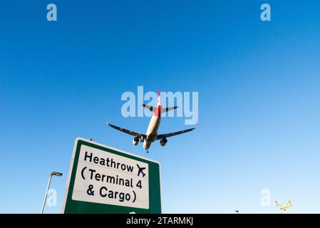 Avion à réaction de ligne en finale pour atterrir à l'aéroport de Londres Heathrow, Royaume-Uni, survolant le panneau de signalisation routière avec les indications pour Heathrow terminal 4 & Cargo Banque D'Images