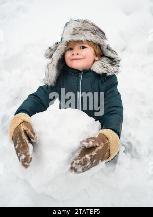 Bonhomme de neige et enfant drôle l'ami est debout dans un chapeau d'hiver et un foulard avec le nez rouge. Joyeux enfant s'amuser avec un bonhomme de neige dans Winter Park. Hiver Banque D'Images