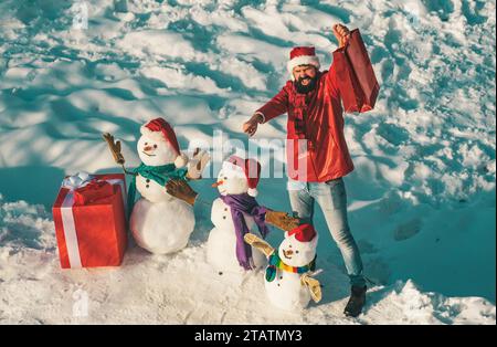 Bel homme d'hiver avec cadeau et bonhomme de neige dans Frosty Winter Park. Drôle Père Noël posant avec boîte cadeau rouge sur le temps d'hiver. Vacances d'hiver et Banque D'Images