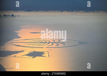 Dubaï, Émirats arabes Unis. 01 décembre 2023. Vue de l'archipel artificiel de Palm Jumeirah dans le golfe Persique d'une hauteur d'environ 2000 mètres. Le rétro-éclairage du soleil bas du soir colore l'eau rougeâtre à orange. Crédit : Soeren Stache/dpa/Alamy Live News Banque D'Images