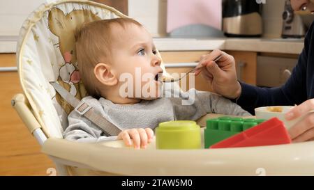 Portrait de bébé garçon souriant heureux devenant désordonné tout en mangeant dans une chaise haute. Concept de parentalité, nutrition saine et alimentation du bébé Banque D'Images