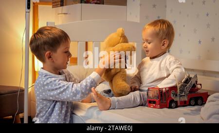 Deux garçons en pyjama jouant avec des jouets dans le lit avant d'aller dormir. Famille ayant du temps ensemble, parentalité, enfance heureuse et divertissement. Banque D'Images