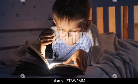 Petit garçon en pyjama étant réveillé la nuit lisant des livres avec une lampe de poche. Éducation des enfants, développement, secret, vie privée, lecture de livres Banque D'Images