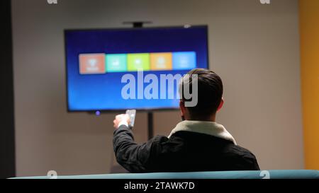 Un jeune homme regardant la télévision et changeant de chaîne avec une télécommande. Banque D'Images