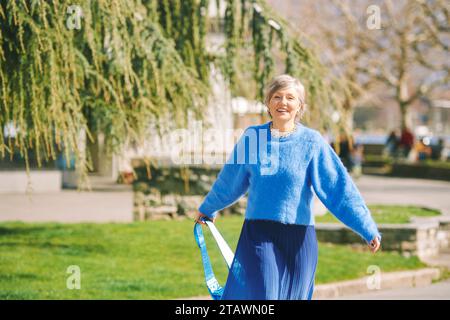 Portrait en plein air de femme mûre heureuse marchant dans la rue par une belle journée ensoleillée, portant des vêtements bleus Banque D'Images