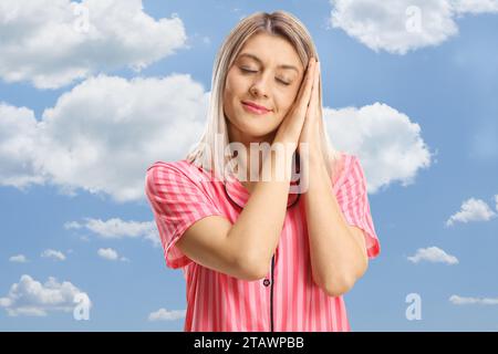 Jeune femme en pyjama dormant parmi les nuages dans le ciel bleu Banque D'Images