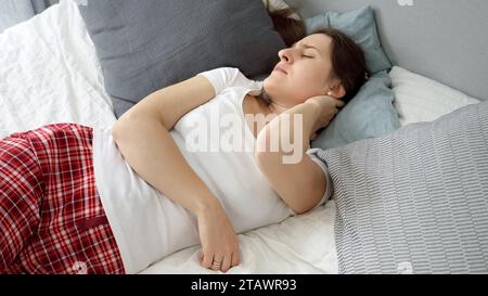 Jeune femme ayant des douleurs dans le cou après avoir dormi sur un oreiller et un matelas inconfortables. Concept de problèmes de santé, soulagement de la douleur et blessures Banque D'Images