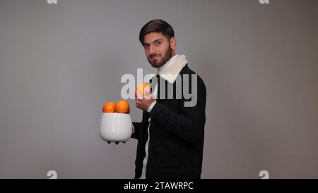 Un jeune homme tenant une orange sur un fond gris | avantages de l'orange Banque D'Images