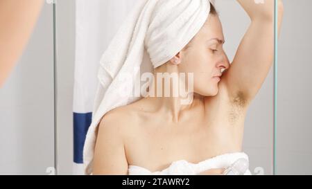 Jeune femme avec de mauvaises aisselles sentent l'utilisation de déodorant de boule pour enlever l'odeur. Concept d'hygiène, de beauté naturelle, de féminité et de croissance des poils du corps Banque D'Images