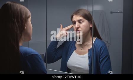 Bouleversée femme stressée regardant dans son reflet dans le miroir et faisant semblant de se tirer dessus dans la tempe avec les doigts. Concept de dépression, suicide, stres Banque D'Images