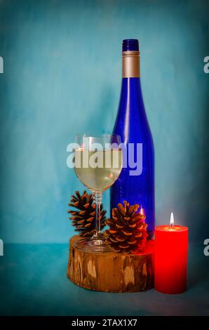 Gros plan d'une bouteille de vin, verre et bougie rouge sur une souche en bois. Bouteille bleue, fond de papier peint Banque D'Images