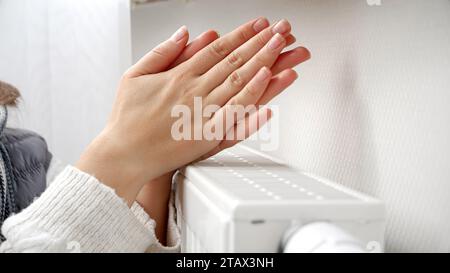 Gros plan d'une femme se sentant col réchauffant ses mains à l'appareil de chauffage mural. Banque D'Images