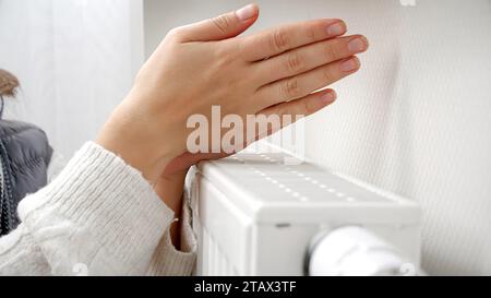 Gros plan de femme réchauffant ses mains au radiateur de chauffage dans la maison. Concept de crise énergétique, factures élevées, système de chauffage cassé, économie et économie d'argent Banque D'Images