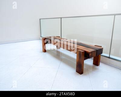 Banc en chêne rustique de coupe épaisse avec personne. Banquette en bois longue épaisse marron vide sur un mur blanc près de la décoration de cloison de verre à l'intérieur du moderne Banque D'Images