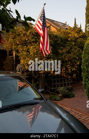 Un drapeau américain pend sous un arbre et se reflète dans la surface brillante du capot d'une automobile. Banque D'Images