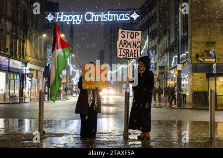 Bradford, Royaume-Uni. 03 DÉCEMBRE 2023. Deux manifestants brandissent des pancartes indiquant "Israel Murders cildren" et "Stop Arming Israel" devant un panneau "Joyeux Noël" à l'extérieur de Centenary Square, Bradford après la conclusion de la Grande Marche de la paix de Bradford et de la Vigile. Crédit Milo Chandler/Alamy Live News Banque D'Images