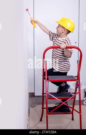 Un constructeur d'enfants se tient sur une échelle et peint les murs blancs d'un appartement. Un enfant avec un rouleau à peinture pendant la rénovation. Banque D'Images