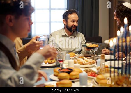 Concentrez-vous sur un homme juif barbu mature offrant à son fils ou à son invité d'essayer des pâtisseries maison traditionnelles tout en tenant une assiette avec de savoureux beignets Banque D'Images